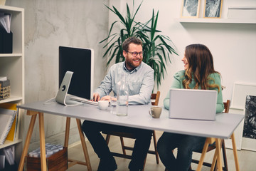 Two coworkers smiling and typing on computer in office.