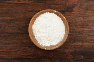 Bowl with flour on wooden table, top view