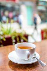 Closeup of white ceramic cup of green black or oolong tea in breakfast outdoor cafe restaurant outside wooden table with patio terrace garden in background