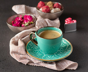 A cup of coffee espresso, sweets and small dried roses in a bowl