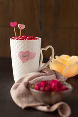 White mug filled with bright pink heart-shaped candies. Rose-shaped candle. Valentine's Day concept. Vertical orientation