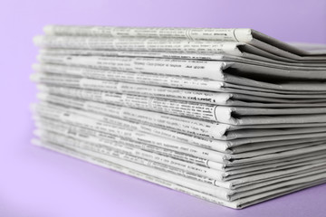 Stack of newspapers on light violet background, closeup. Journalist's work