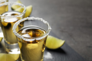 Mexican Tequila shots with salt and lime slices on grey table, closeup. Space for text