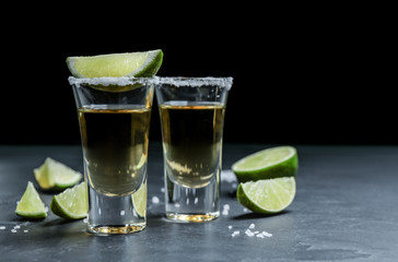 Mexican Tequila shots with salt and lime slices on grey table. Space for text