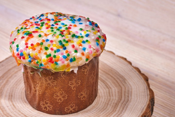 Easter composition. Easter cake on a stand made of a slice wood on a light wooden background. Close-up