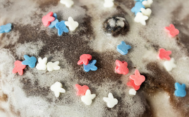 Sugar colored confetti lies on a white icing cupcake, texture of sugar icing on a cupcake surface close-up, pink, blue and white candy