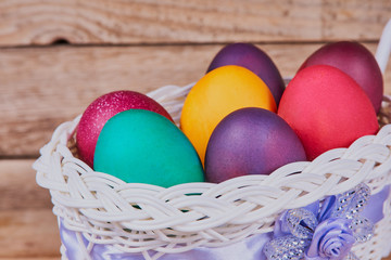 Easter composition. White basket on wheels with colorful Easter eggs on a wooden background. Close-up