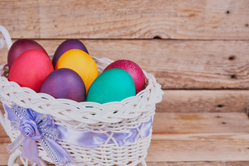 Easter composition. White basket on wheels with colorful Easter eggs on a wooden background. With copy space