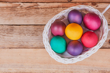 Easter composition. White basket on wheels with colorful Easter eggs on a wooden background. Flat lay