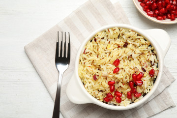 Tasty rice pilaf with pomegranate grains served on white wooden table, flat lay