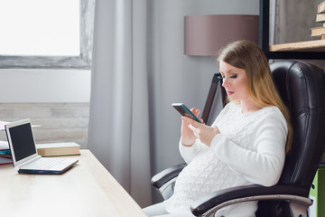 Pregnant woman working on laptop. business lady at work. pregnancy, business, work and technology concept. Abdomen girl working with smartphone at table in office in third trimester