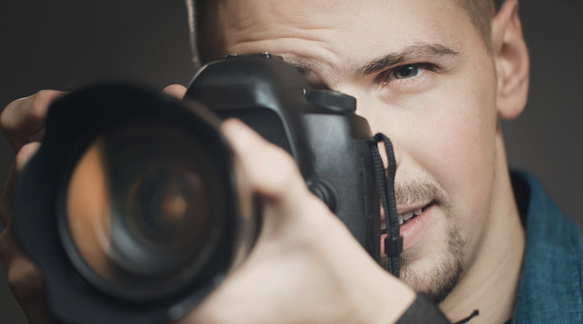 Close-up of photographer looking in his camera viewfinder, focus on man's face, isolated dark background