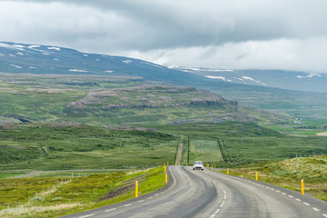 Fototapeta premium Ring road in east Iceland highway with green landscape and car on steep slope with overcast cloudy stormy weather near Egilsstad