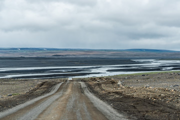 Dirt road in Iceland highway 864 to Dettifoss with barren brown landscape on cloudy day and volcanic lava field with fjord