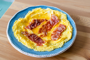 Omelette with Prosciutto Ham Jamon Crudo in Breakfast Plate on Wooden Kitchen Table.