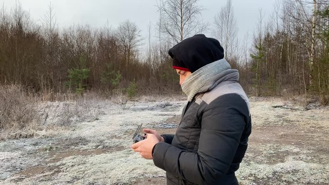 Young man controls a drone through a remote control. Launch of an unmanned aerial vehicle in the winter forest. Quadrocopter observation.