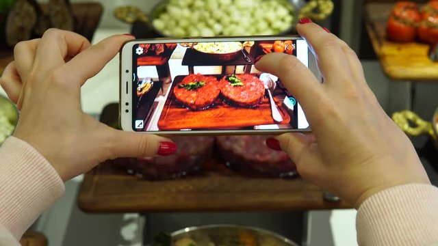 A woman photographs food in a restaurant buffet. A blogger makes a photo with a smartphone for social networks. Technology and luxury holiday concept.