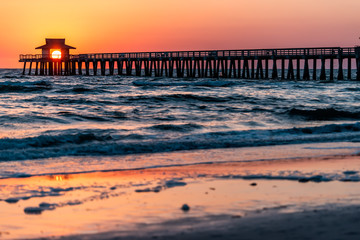 Naples, Florida colorful red vibrant sunset in gulf of Mexico with sun path reflection and Pier wooden jetty silhouette with horizon and ocean waves