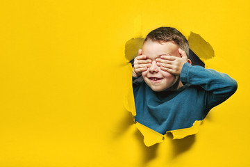 Happy cute boy is having fun played on black background wall. climbs through a hole in the paper. Bright photo of a boy.