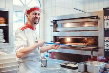 Smiling chef putting pizza in the oven in a restaurant kitchen