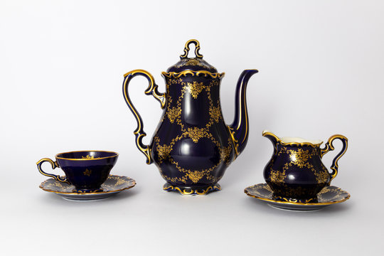 Closeup of a beautiful cobalt blue colored vintage porcelain tea set with golden floral pattern on white background. The set includes a tea pot, a milk jug and a tea cup.