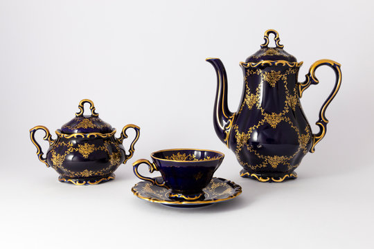 Closeup of a beautiful cobalt blue colored vintage porcelain tea set with golden floral pattern on white background. The set includes a tea pot, a sugar bowl and a tea cup.
