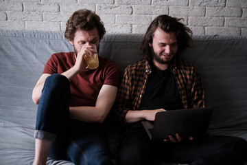 Gay couple sitting together on the sofa while one works on the laptop.