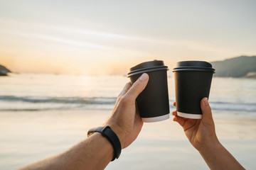 Two disposable paper cups in the hands of a man and a woman against the backdrop of a beautiful...