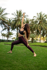  A girl practicing yoga on a beautiful tropical grass field surrounded by palm trees