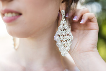 Large earrings with pearls in the shape of a rhombus on the girl’s ear. Bride's hand near stylish earrings