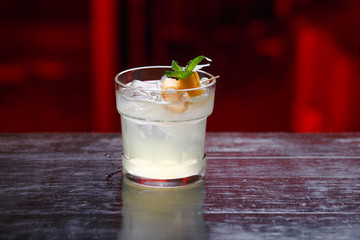 Closeup of a lemon and gin cocktail in short glass, standing on the bar counter, isolated on a red light background.