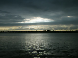 Beautiful Sun Rays of bright light shining through hole of dark clouds and illuminating lake water horizon in sunset time. Dramatic Texas sky atmosphere. Beauty in nature background.