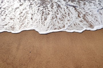A downward shot of a foamy waters edge on sand