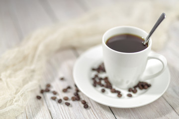 Close up a cup of hot coffee with roasted coffee beans on white wooden table.