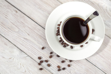 Close up a cup of hot coffee with roasted coffee beans on white wooden table.
