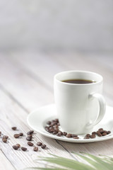 Close up a cup of hot coffee with roasted coffee beans on white wooden table.