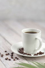 Close up a cup of hot coffee with roasted coffee beans on white wooden table.