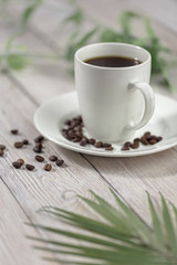 Close up a cup of hot coffee with roasted coffee beans on white wooden table.