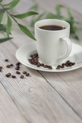 Close up a cup of hot coffee with roasted coffee beans on white wooden table.
