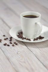 Close up a cup of hot coffee with roasted coffee beans on white wooden table.