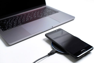 phone on a wireless charger next to a computer on a white table