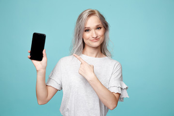 Cheerful female person in the t-shurt pointing phone in the blue studio