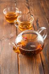Knitted blooming tea in a transparent teapot close-up. Tea ceremony on a dark wooden background and copy space.