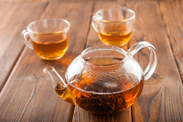 Knitted blooming tea in a transparent teapot close-up. Tea ceremony on a dark wooden background and copy space.