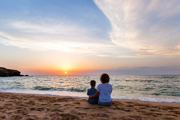 family vacation. Travelers mother and son are sitting in the summer on the ocean and watching the sunset. back view