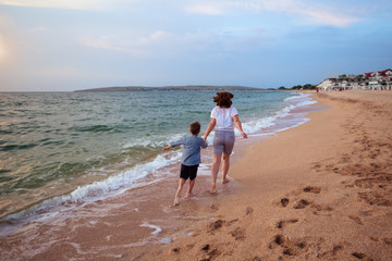 Summer vacation for family travelers. mother and son are running along the seashore. The view from the back.