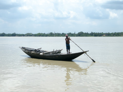 Traditional boatman (ferry people Majhi) rowing boat (called Nauka) on river Ganges (Ganga). Rural Indian travel tourism and water transportation theme. The Sundarbans West Bengal India South Asia Pac
