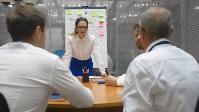 Young attractive confident business woman speaker makes speech to company leaders. Project manager doing presentation to clients or workers group at conference meeting office team in boardroom