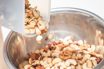 Pour hazelnuts, almonds, cashews and a walnut in one bowl with cashews to create an assortment of nuts for a balanced diet.