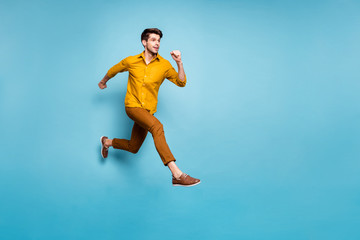 Fototapeta na wymiar Full length profile photo of funny excited guy jumping high running speed almost get finish line wear yellow shirt pants isolated blue color background